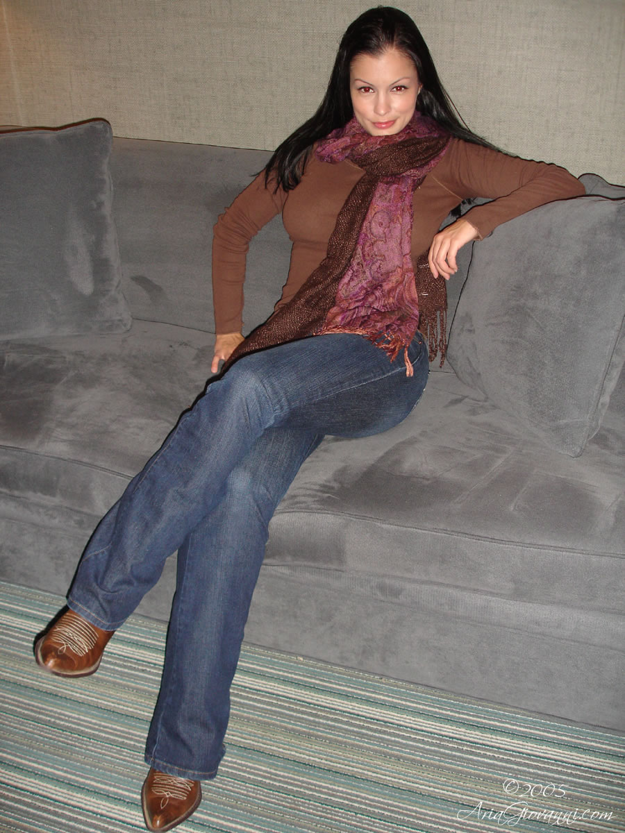 aria_giovanni breasts brown_hair female jeans large_breasts long_hair scarf shoes sitting smile sofa solo