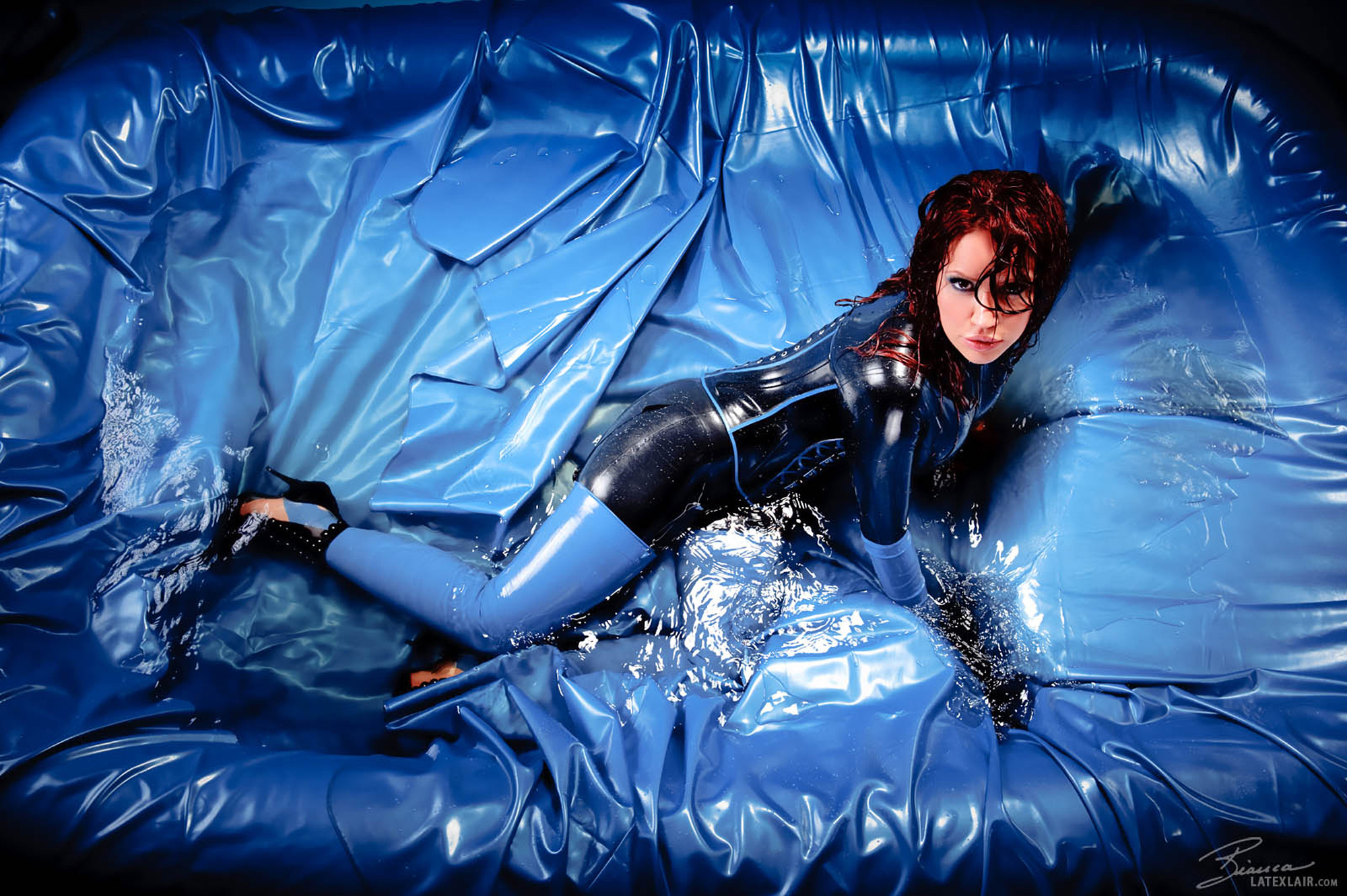 bed bianca_beauchamp breasts catsuit corset female gloves high_heels large_breasts latex long_hair red_hair shoes solo thighhighs watermark