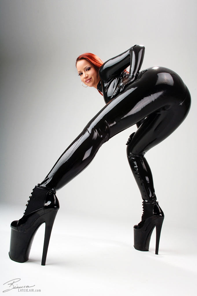 ass bianca_beauchamp breasts catsuit earrings female high_heels large_breasts latex long_hair looking_back red_hair shoes simple_background solo watermark