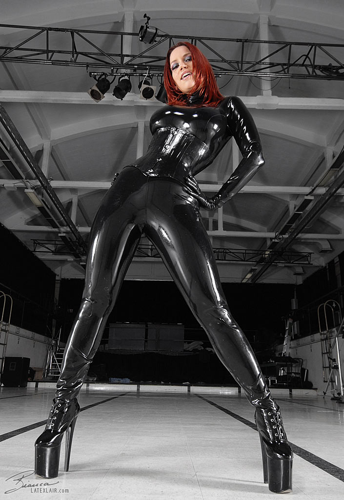 bianca_beauchamp breasts catsuit female gloves high_heels large_breasts latex long_hair red_hair shoes solo watermark