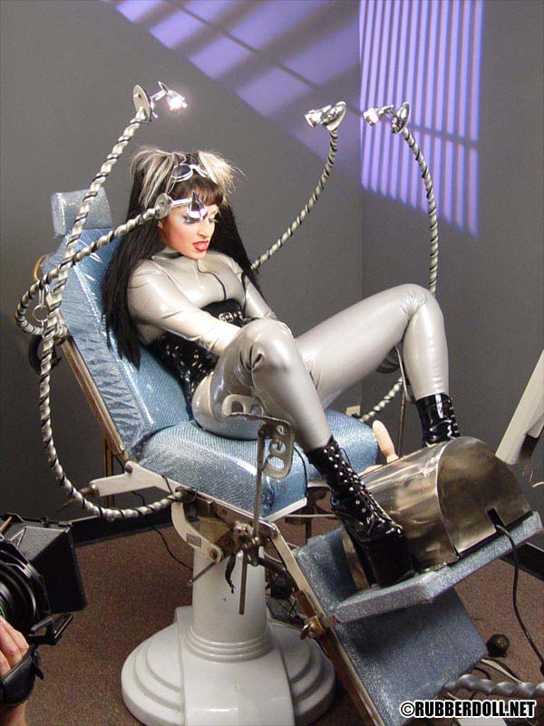 black_hair boots catsuit chair corset female high_heels latex long_hair rubberdoll sitting solo