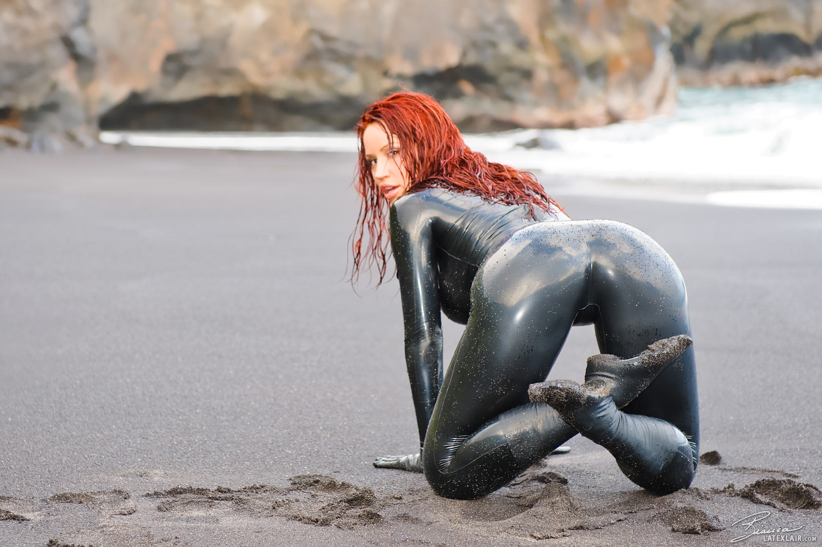 ass beach bianca_beauchamp breasts catsuit female gloves high_heels large_breasts latex long_hair looking_back outside red_hair sand shoes solo water watermark wet
