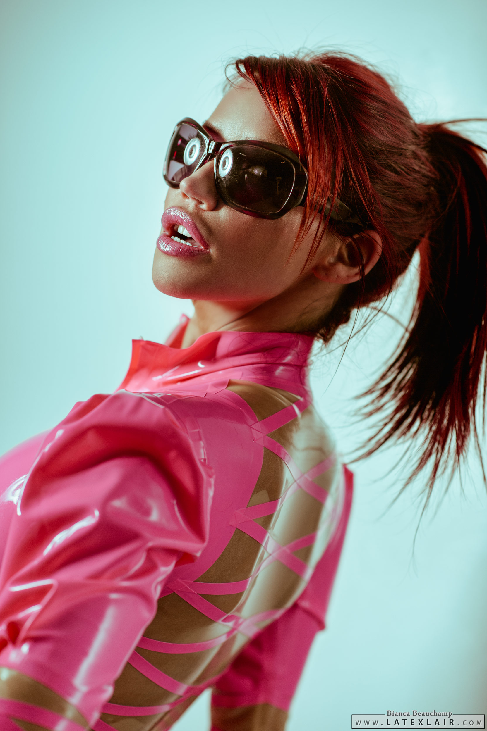 bianca_beauchamp breasts female large_breasts latex long_hair looking_back ponytail red_hair simple_background solo sunglasses