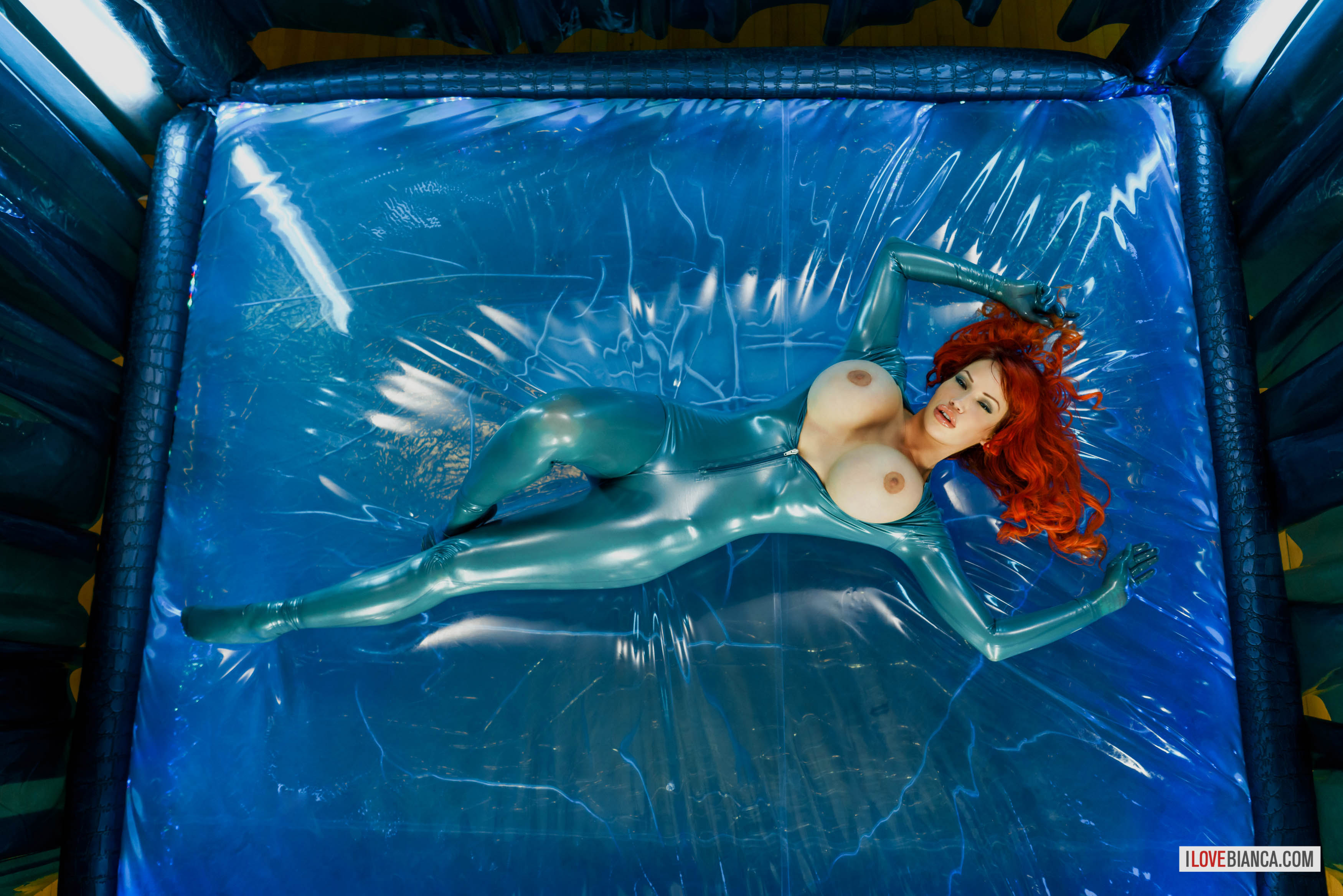 bed bianca_beauchamp breasts catsuit female high_heels large_breasts latex long_hair red_hair shoes solo watermark