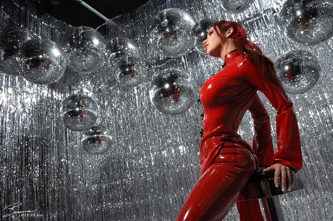 ass bianca_beauchamp breasts catsuit disco_ball female large_breasts latex long_hair looking_back red_hair solo