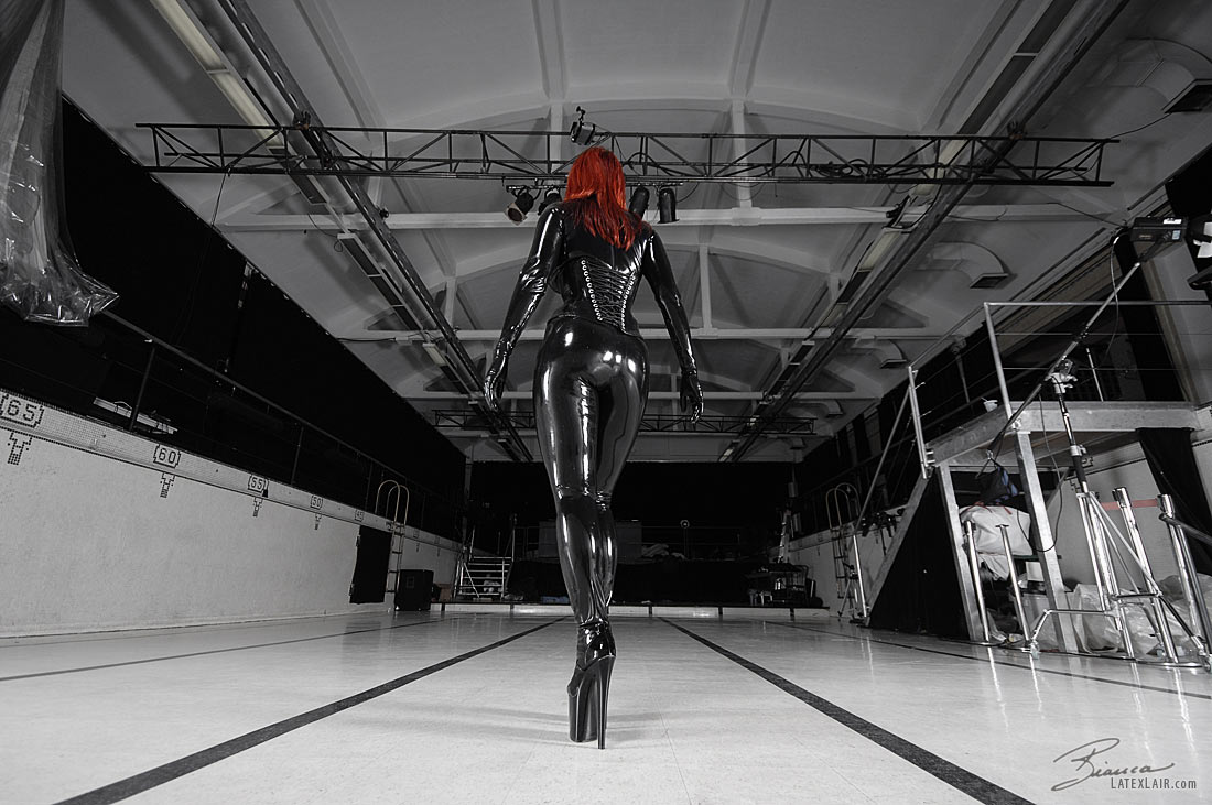 ass bianca_beauchamp breasts catsuit female gloves high_heels large_breasts latex long_hair looking_back red_hair shoes solo watermark