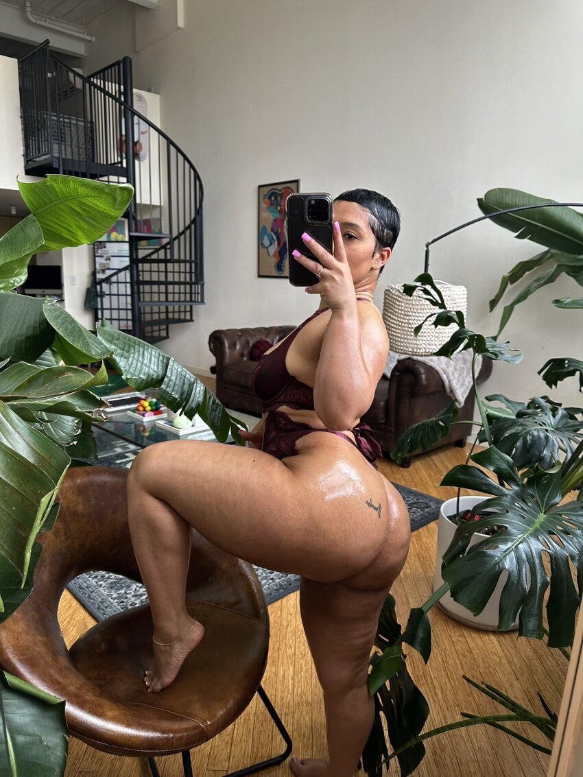 1girl amberthickk big_ass black_female curvy_thighs female female_only foot_on_chair holding_phone leg_up lingerie living_room mirror_selfie painted_nails phone ring selfie shiny_ass short_hair solo tattoo_on_ass