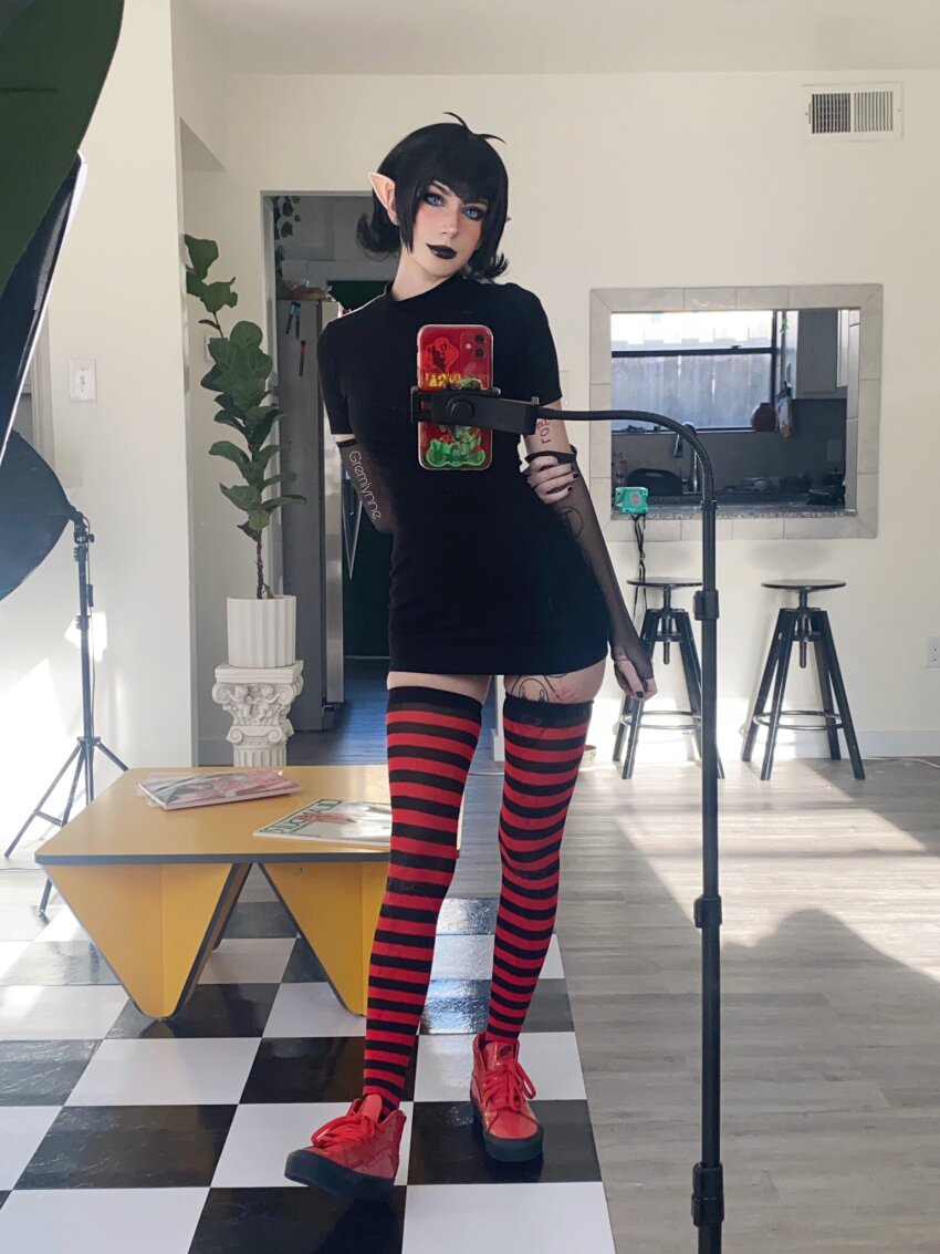 1girl black_hair black_lipstick cosplay gremlynne hotel_transylvania mavis_dracula pointy_ears solo standing striped_legwear tattoo