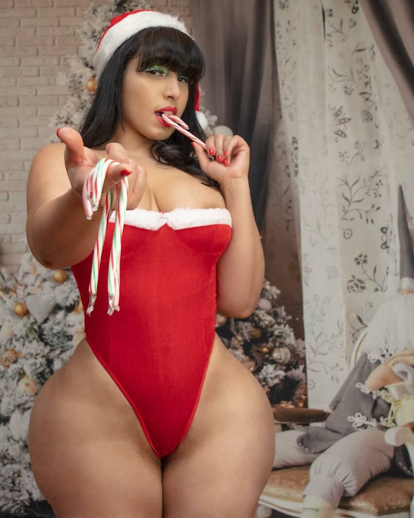 1girl ass bangs bare_shoulders blunt_bangs bottom_heavy breasts bubble_butt candy candy_cane christmas clothed dat_ass eating female female_only hat holidays huge_ass instagram latina leotard lipstick looking_at_viewer medium_breasts nail_polish natural_breasts nipple_slip pointing pointing_at_viewer red_lipstick red_nails santa_hat solo standing stephanie_rodriguez thong_leotard wide_hips