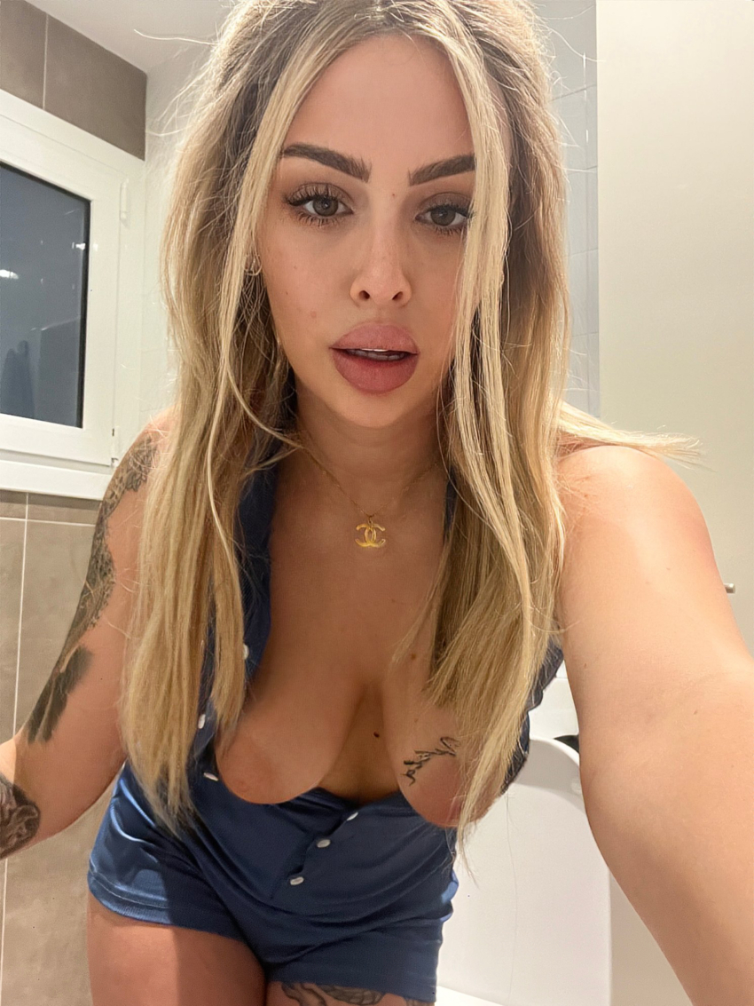 blonde_hair breasts_out brown_eyes leaning_forward lipstick long_hair looking_at_viewer lya_missy necklace selfie shorts spanish_female tattoos