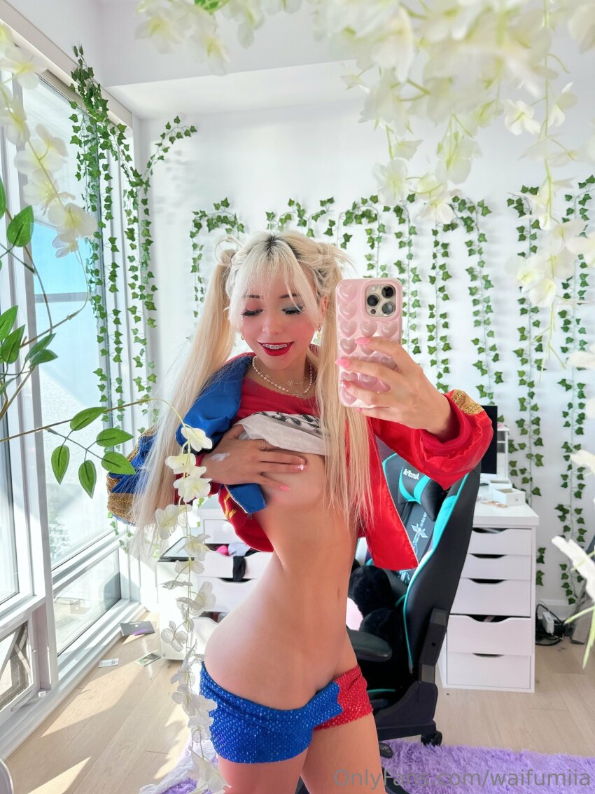 1girl asian asian_female blonde blonde_female blonde_hair closed_eyes cosplay covering_breasts dc dc_comics harley_quinn harley_quinn_(cosplay) highres izzybunnies mirror_selfie onlyfans photo revealing revealing_clothes selfie sexually_suggestive shorts slim solo solo_female solo_focus suggestive twintails underboob undressing waifumiia watermark