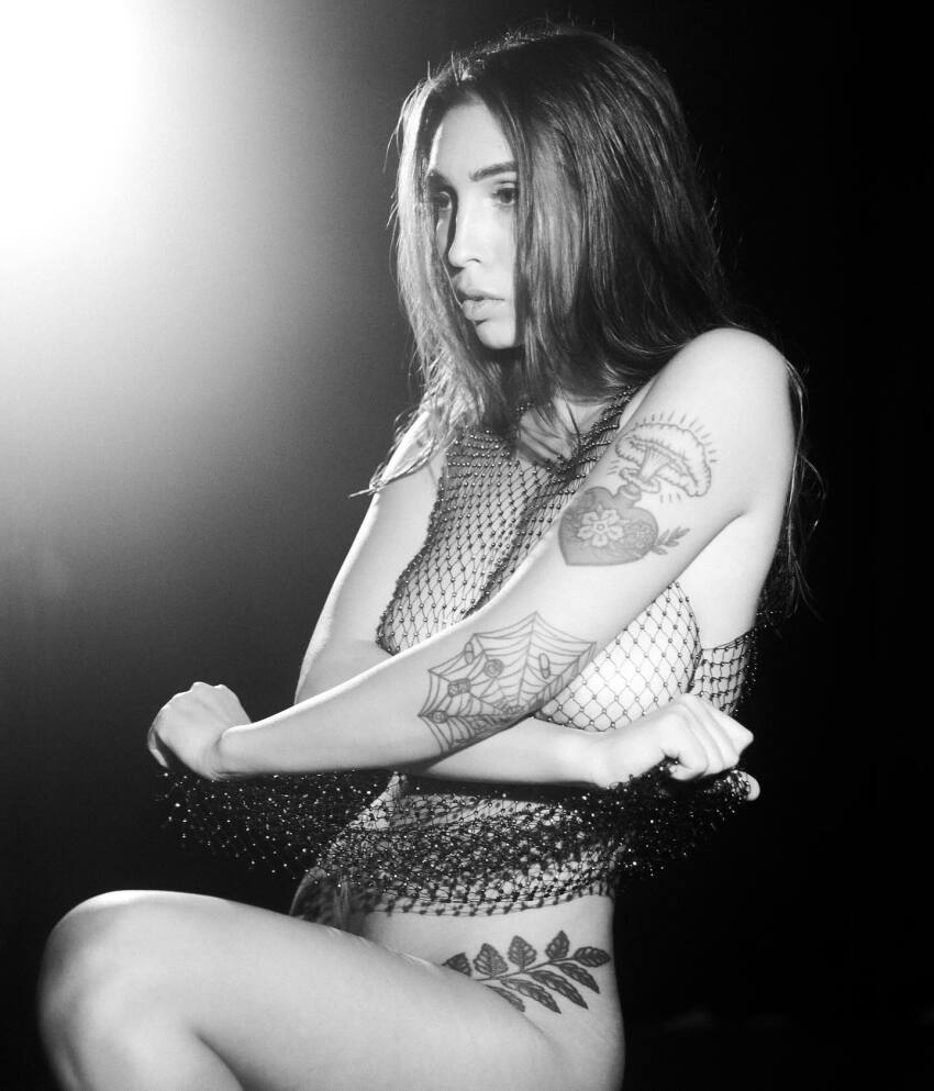 1girl aisultana breasts female female_focus female_only female_solo looking_at_viewer medium_breasts monochrome sitting solo solo_female solo_focus tattoo tattoo_on_arm tattoo_on_leg