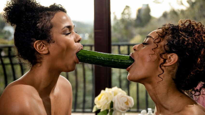 2girls alina_li black_female bun closeup cucumber curly_hair dark-skinned_female digitalplayground ebony eyes_closed food food_in_mouth food_play highres no_sex non-nude oral phallic photo pornstar scarlit_scandal sexually_suggestive sfw sourced suggestive_food tied_hair