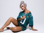 1girl barefoot bimbo breasts caucasian christie_hagan clothed curvy eyelashes female female_only football_jersey full_lips hips jersey knee_up legs looking_at viewer milf model necklace non-nude posing ring sitting sourced tan_skin tattoo thick_thighs tied_hair toned white_hair